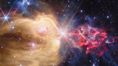 James Webb Space Telescope NIRCam infrared view of the stellar nursery NGC 7129, showing a golden cavity carved by outflows from the star LkHa 234 and reddish clumpy clouds hiding young protostars.