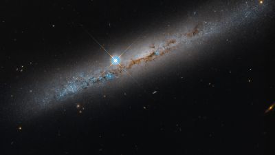 Hubble image of the edge-on spiral galaxy NGC 1827, its bright disk crossed by dark dust lanes and blue star-forming regions, with a foreground star showing diffraction spikes.