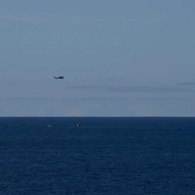 Three U.S. Navy MH-60 Seahawks from Helicopter Sea Combat Squadron (HSC) 23 flies overhead as small boats approach NASA’s Orion...
