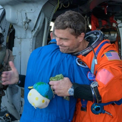 NASA astronaut Reid Wiseman, Artemis II commander, gives NASA Flight Surgeon Richard Scheuring a hug next to a Navy MH-60...