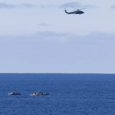 A U.S. Navy MH-60 Seahawks from Helicopter Sea Combat Squadron (HSC) 23 flies overhead as small boats approach NASA’s Orion...
